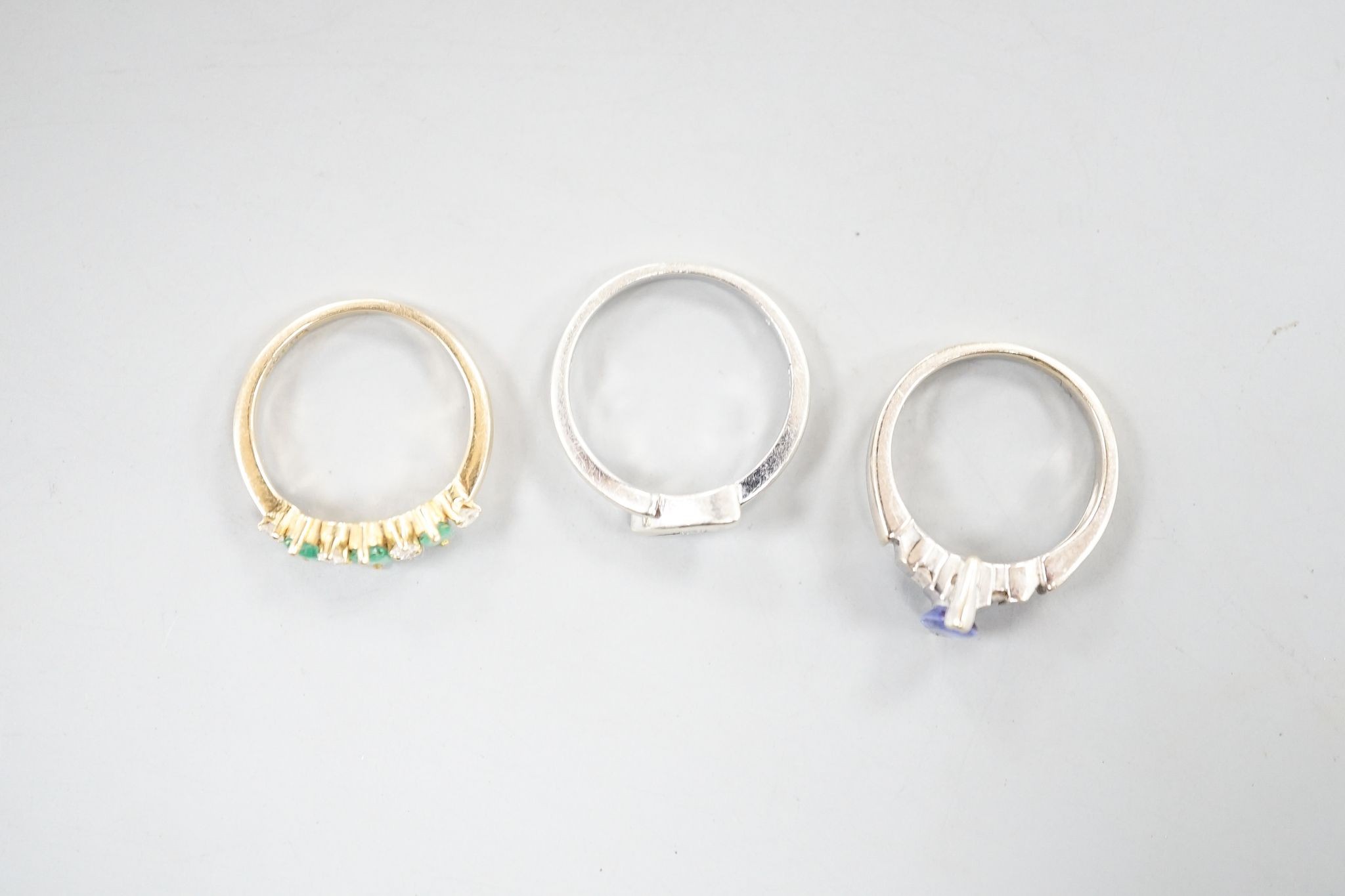 A 750 yellow metal, three stone emerald and six stone diamond chip set half hoop ring, size L, a 750 white metal and tanzanite ring, size K, gross 6.4 grams and a 9ct white gold and diamond chip set ring, gross 2.4 grams